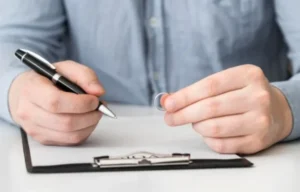A man writing on a clipboard with a pen, while holding a ring.