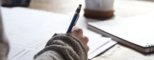 A focused person sitting at a desk, writing notes on a paper with a pen.