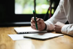 A person writing on a notebook with a pen, capturing thoughts and ideas on paper.