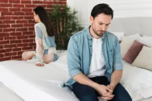 A man and a woman sitting on opposite sides of a bed.