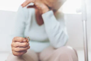 An elderly woman holding a wedding ring, while crying.