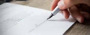 A person signing a contract on a piece of paper with a pen.