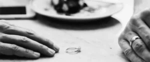 Two hands resting on a table with wedding rings
