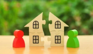 A wooden house puzzle broken in the middle with two wooden people separated by each side.