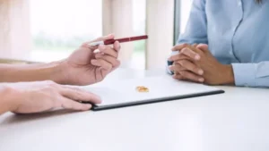 A person hands a pen and a contract with a ring to the other.