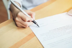 A woman signing a contract with a pen on a table.