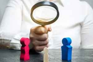 A person using a magnifying glass to examine a wooden figure closely.