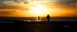 Two individuals strolling on a sandy beach during sunset, enjoying the serene beauty of the moment.