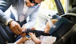 A well-dressed man assisting a baby in a car seat.