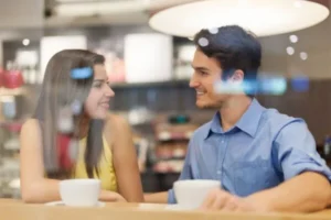 A man and woman sitting at a table in a coffee shop, enjoying a conversation over cups of coffee.