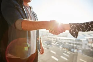 A man and woman shaking hands in front of a window.