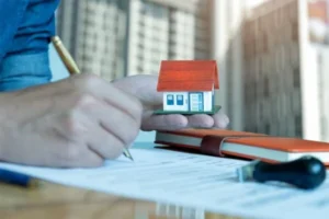 A man signing a contract while holding a model of a house