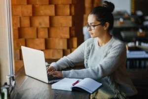 A woman wearing glasses is focused on her laptop.