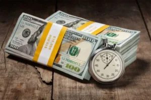 A stopwatch and money stack on a wooden table.