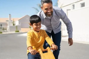 A man and boy happily riding a wooden toy car together in a park.