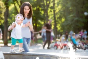 A woman and child standing in front of a fountain in a park.
