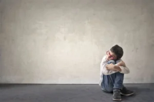 A young boy sitting on the floor with his arms crossed.