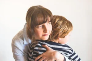 A woman lovingly embraces a child wearing a striped shirt.