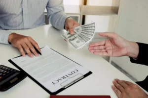 A person filling out a contract and giving out money to another person
