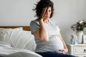A pregnant woman sitting on a bed in her bedroom.
