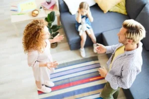 A man and woman engage in conversation and a child while in a cozy living room setting.