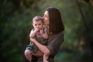 A woman holding a baby in a serene forest setting.