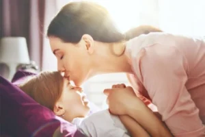 A mother tenderly kissing her daughter on the forehead