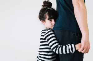 A young girl with pigtails hugs her father's leg
