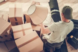 A man packing boxes in a room with a lamp, preparing for a move or storage.