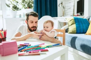 A man and a baby sitting at a table with markers.