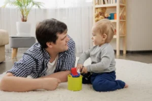 A man and a baby happily playing with toys on the floor.