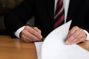 A man in a suit is signing documents while flipping through the pages.