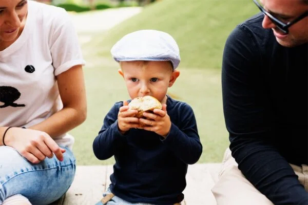 A man and woman sitting on the ground with a child eating a sandwich.