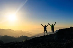 Two hikers with their hands lifted, relishing the sunrise view from the mountain.