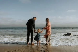 A family of three enjoying a sunny day at the beach, playing in the sand and splashing in the water.