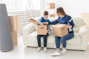 A woman and boy sitting on a couch surrounded by moving boxes.