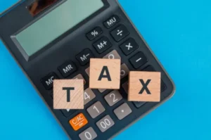 Wooden blocks arranged to form a tax on top of a calculator on a blue background