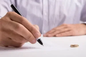 A man signing a document with a pen and a ring on the table.