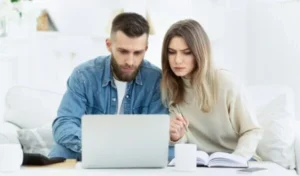 A man using his laptop while a woman holds a pen and looks at his screen