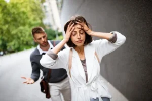 A woman and a man are arguing; the woman is holding her head in frustration.