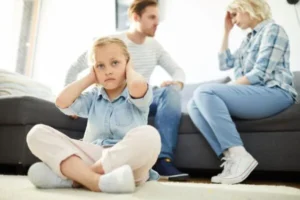 A couple is sitting on the couch arguing while their son sits on the floor, covering his ears.