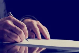 A man signing a document with a black background.
