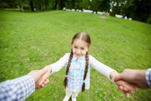 A little girl holds her father's hand while standing on the grass.n green grass.
