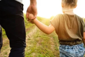 A father is holding his daughter as they walk together toward the grassy field.