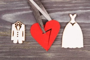 Cut-out paper shapes of a wedding dress and suit, with a broken red heart and scissors in the center