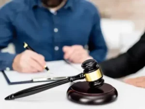 A judge's gavel on a desk in front of two men, one wearing a suit and the other in casual attire.
