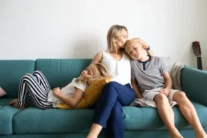 A woman kisses her son on the head while sitting on the couch with her daughter