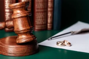 A gavel and books are placed alongside a couple's ring with a piece of paper underneath it.