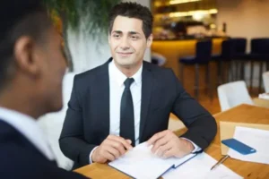 A man in a suit sitting at the table, listening and smiling at someone.