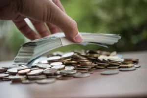 A hand holding cash with a backdrop of coins.